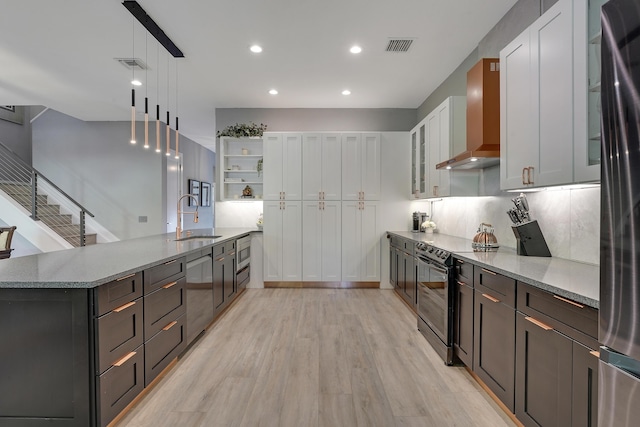 127 Via Castilla, Jupiter, FL 33458 - kitchen featuring stainless steel appliances, a sink, wall chimney range hood, light stone countertops, and light wood-type flooring
