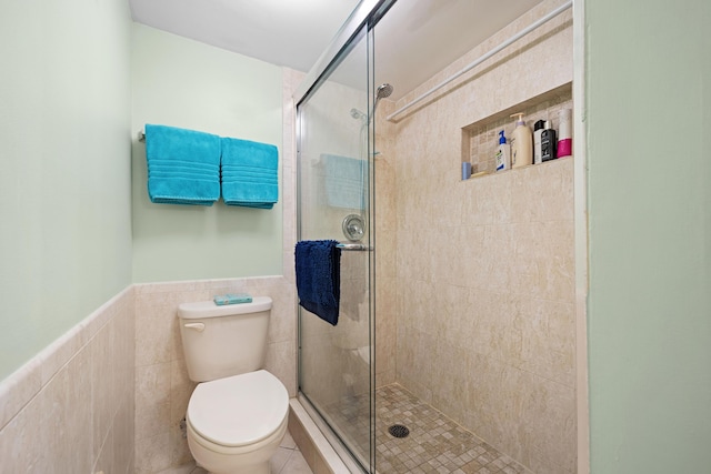 bathroom with a shower stall, tile walls, toilet, and wainscoting