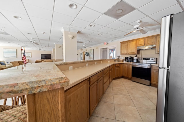kitchen featuring stainless steel appliances, open floor plan, under cabinet range hood, a kitchen breakfast bar, and light tile patterned floors