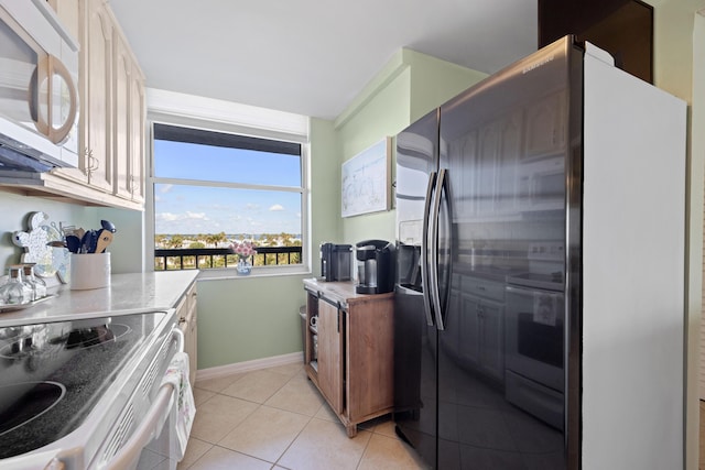 kitchen with white microwave, range with electric stovetop, stainless steel refrigerator with ice dispenser, baseboards, and light tile patterned floors