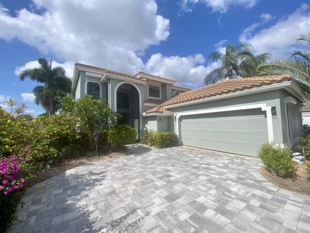 mediterranean / spanish-style house featuring stucco siding, an attached garage, decorative driveway, and a tiled roof