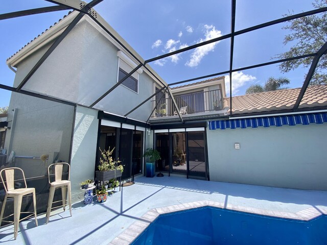back of house featuring a balcony, a patio, stucco siding, a lanai, and an outdoor pool