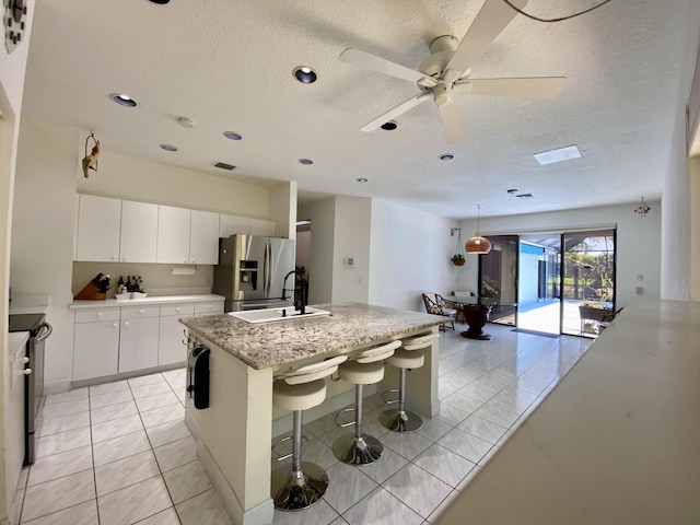 kitchen featuring stainless steel fridge, a sink, a kitchen island with sink, a textured ceiling, and white cabinetry