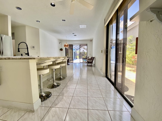 kitchen with a textured ceiling, ceiling fan, a breakfast bar, a textured wall, and light stone countertops