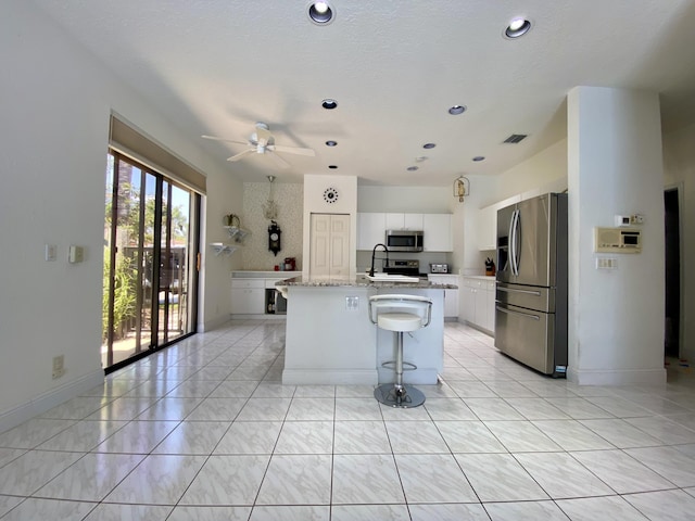 10039 Lexington Cir N, Boynton Beach, FL 33436 - kitchen featuring appliances with stainless steel finishes, a ceiling fan, a kitchen island with sink, white cabinetry, and a breakfast bar area