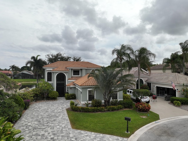 mediterranean / spanish-style home featuring decorative driveway, a tile roof, stucco siding, a front yard, and an attached garage