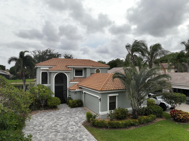 mediterranean / spanish-style home featuring an attached garage, decorative driveway, a tile roof, and stucco siding