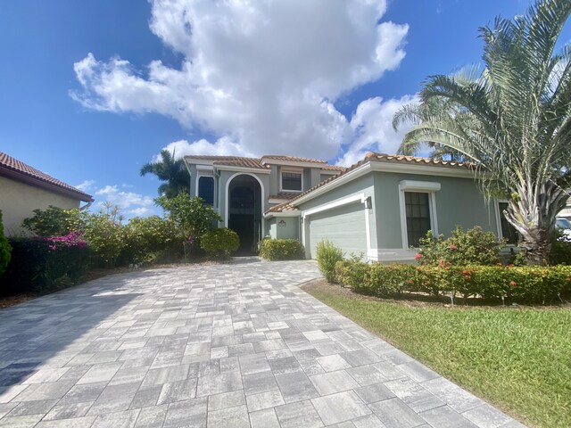 mediterranean / spanish-style house with decorative driveway, an attached garage, stucco siding, and a tiled roof