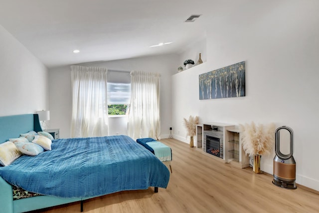 bedroom featuring vaulted ceiling, wood finished floors, baseboards, a glass covered fireplace, and recessed lighting