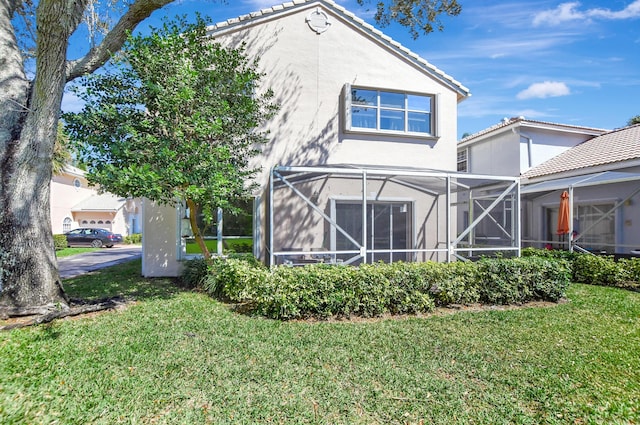 back of property with a yard, stucco siding, a tile roof, and a lanai