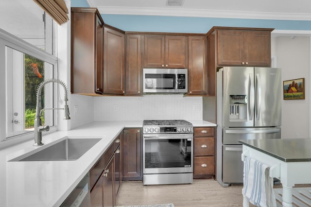 765 Lagoon Dr, North Palm Beach, FL 33408 - kitchen featuring stainless steel appliances, a sink, backsplash, ornamental molding, and light wood-type flooring