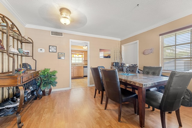 dining area with light wood-style flooring, a textured ceiling, ornamental molding, and baseboards
