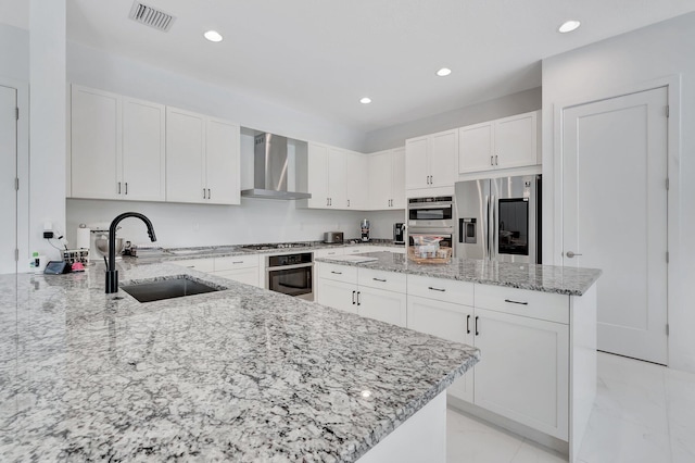 kitchen featuring wall chimney range hood, a sink, stainless steel appliances, light stone counters, and recessed lighting