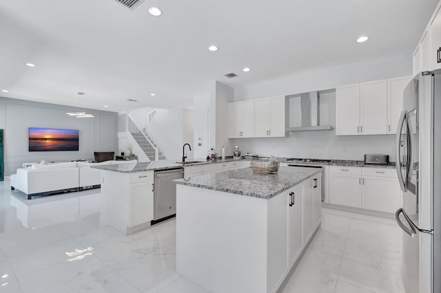 kitchen featuring appliances with stainless steel finishes, wall chimney exhaust hood, light marble finish flooring, a sink, and recessed lighting