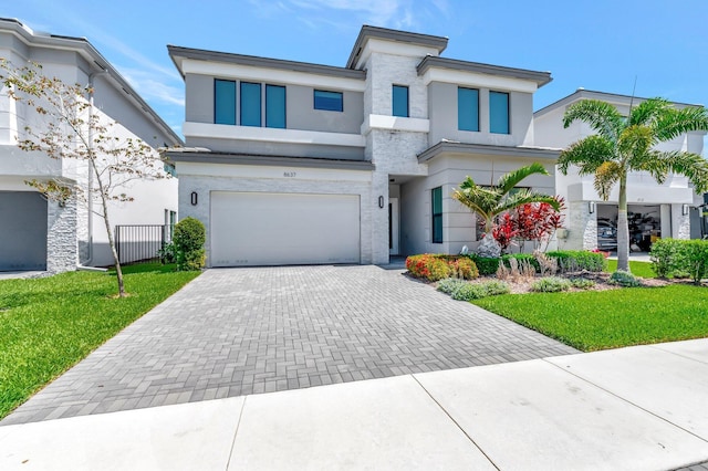 modern home with stucco siding, a garage, decorative driveway, and stone siding