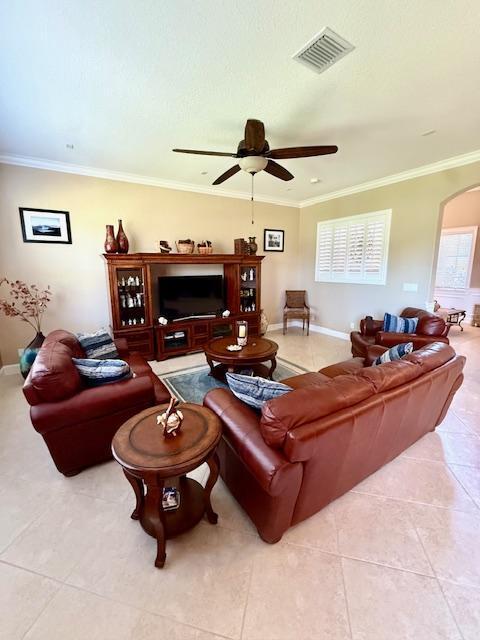 living room with arched walkways, light tile patterned flooring, a ceiling fan, ornamental molding, and healthy amount of natural light