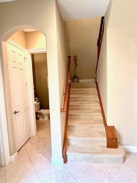 staircase featuring arched walkways, tile patterned floors, and baseboards