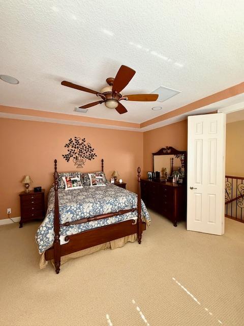 bedroom featuring light colored carpet, a textured ceiling, ceiling fan, and baseboards