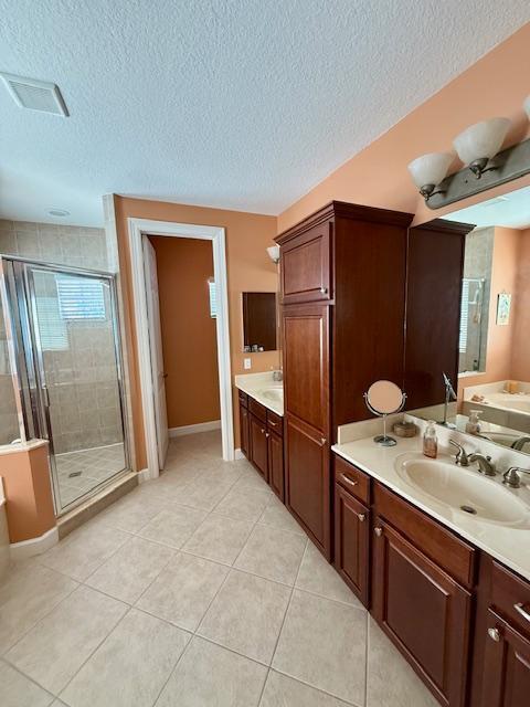 bathroom with a stall shower, baseboards, a textured ceiling, tile patterned flooring, and two vanities