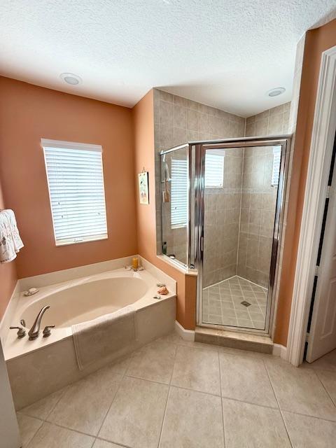 full bath with tile patterned floors, a textured ceiling, a garden tub, a shower stall, and baseboards
