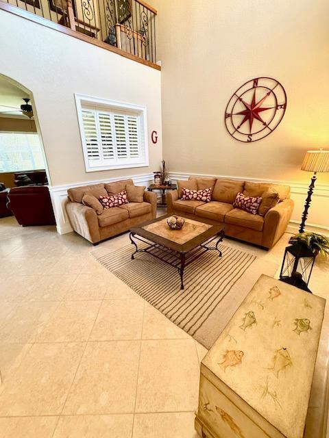 living room featuring wainscoting, ceiling fan, a decorative wall, tile patterned flooring, and a high ceiling