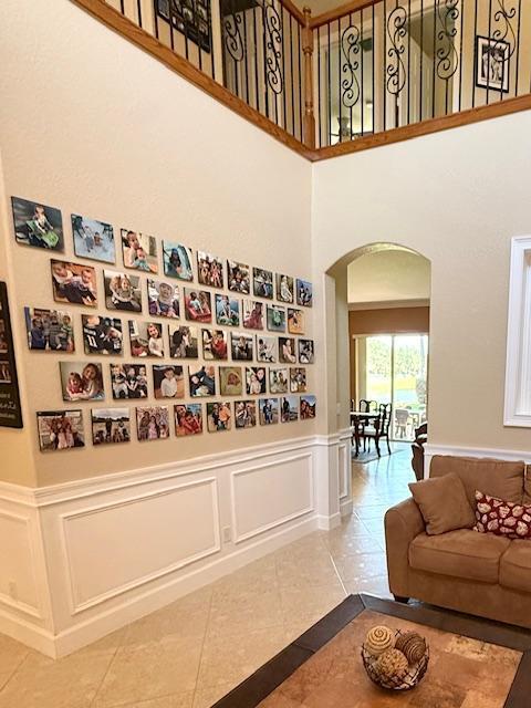 hall featuring arched walkways, a high ceiling, a wainscoted wall, a decorative wall, and tile patterned floors