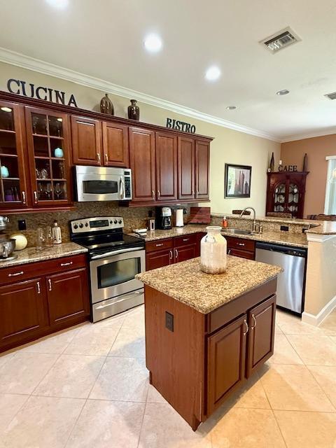 kitchen featuring stainless steel appliances, a sink, decorative backsplash, light tile patterned floors, and ornamental molding