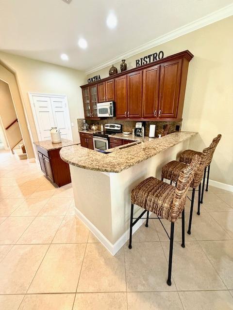kitchen featuring appliances with stainless steel finishes, a peninsula, a kitchen bar, ornamental molding, and light tile patterned floors