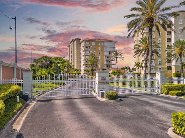 view of asphalt road with street lighting, a gate, curbs, and a gated entry
