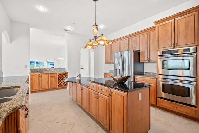 kitchen with appliances with stainless steel finishes, a kitchen island, arched walkways, light tile patterned flooring, and dark stone counters
