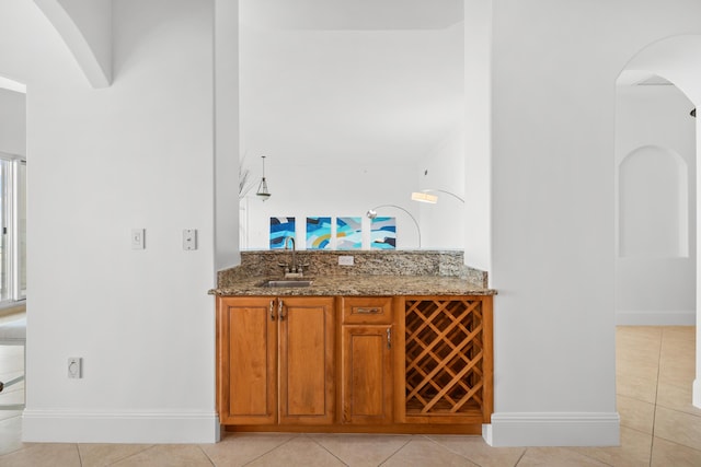 bar featuring a sink, light tile patterned flooring, arched walkways, and baseboards