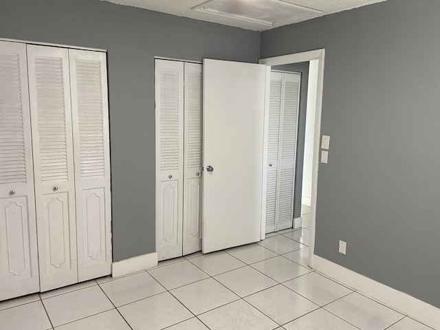 unfurnished bedroom with two closets, attic access, light tile patterned flooring, and baseboards