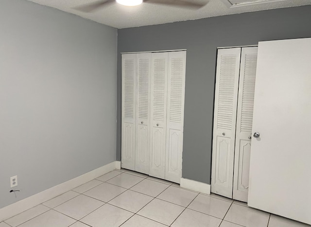 unfurnished bedroom featuring multiple closets, baseboards, light tile patterned floors, and ceiling fan
