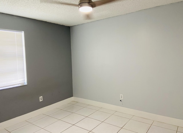 empty room with a textured ceiling, light tile patterned floors, and baseboards