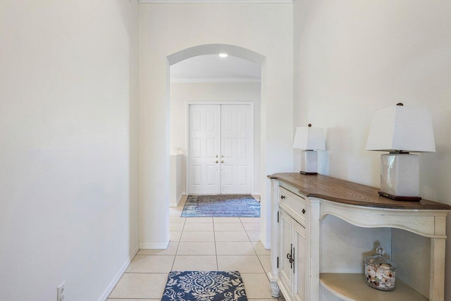 hallway featuring arched walkways, crown molding, light tile patterned flooring, and baseboards