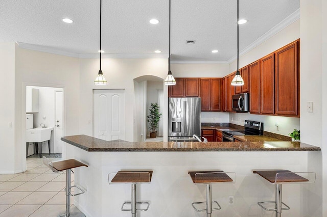 kitchen with appliances with stainless steel finishes, a textured ceiling, a peninsula, arched walkways, and a kitchen breakfast bar