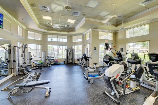 gym with a ceiling fan, ornamental molding, healthy amount of natural light, a raised ceiling, and a towering ceiling