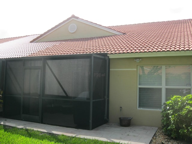 rear view of property with a tiled roof, a sunroom, and stucco siding