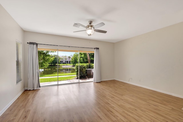empty room with a ceiling fan, a water view, light wood finished floors, and baseboards