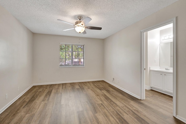 unfurnished bedroom featuring wood finished floors, a textured ceiling, a sink, baseboards, and ensuite bathroom