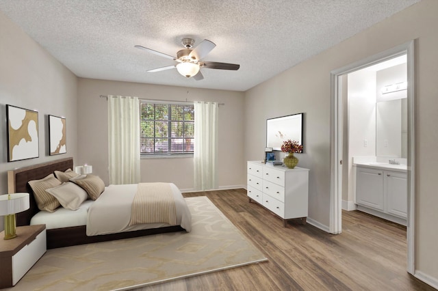 bedroom featuring light wood-type flooring, a textured ceiling, a sink, connected bathroom, and baseboards