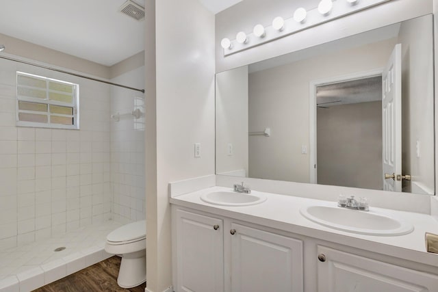 bathroom featuring toilet, a tile shower, double vanity, and wood finished floors