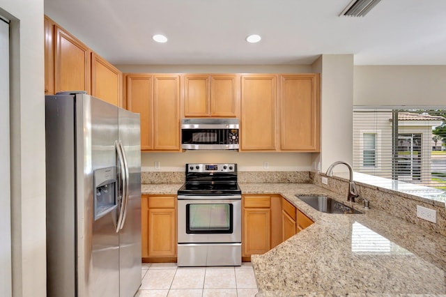 kitchen with stainless steel appliances, a sink, light brown cabinets, light tile patterned floors, and light stone countertops