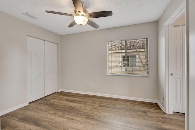 unfurnished bedroom featuring wood finished floors, baseboards, a closet, and a textured ceiling