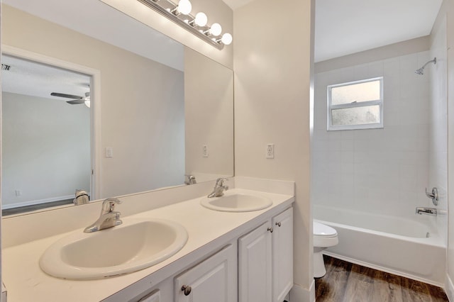 bathroom featuring toilet, wood finished floors, bathing tub / shower combination, a ceiling fan, and double vanity