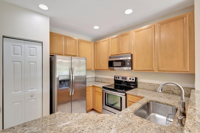 kitchen with appliances with stainless steel finishes, a sink, light brown cabinets, light stone counters, and recessed lighting