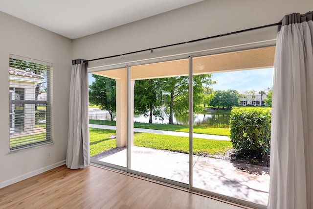 doorway with a water view, healthy amount of natural light, wood finished floors, and baseboards