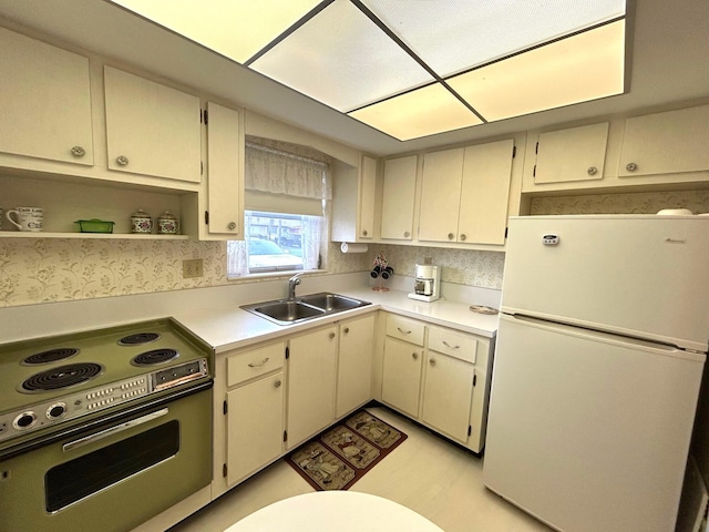 kitchen with freestanding refrigerator, a sink, stainless steel range with electric cooktop, light countertops, and cream cabinets