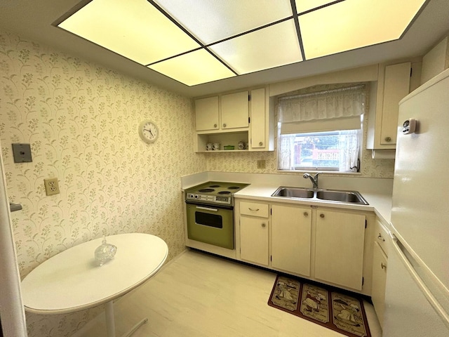 kitchen with electric range oven, a sink, light countertops, freestanding refrigerator, and cream cabinets