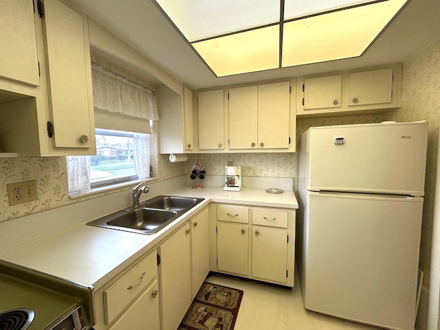 kitchen with freestanding refrigerator, a sink, cream cabinets, and light countertops